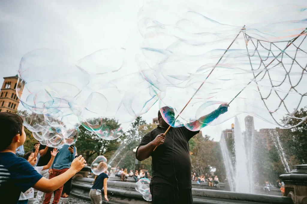 man and children making large bubbles with bubble sticks